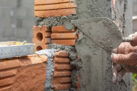 Man applying mezcla para pegar ladrillos con una paleta. Se ve una regla de albañil.