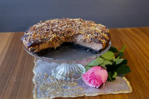 En läcker choklad cheesecake med chokladspån och nötter, serverad med en rosa ros.