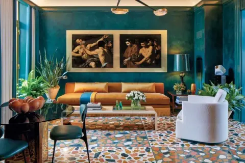 Soggiorno con divano arancione, quadri classici e pavimento a terrazzo. La differenza tra ottanio e petrolio è evidente nei toni del muro e delle tende.