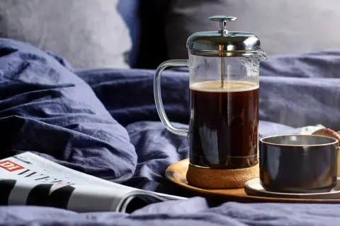 En franskpress med kaffe bredvid en tidning och en kopp. En lugn morgon med kaffe, inte espresso.