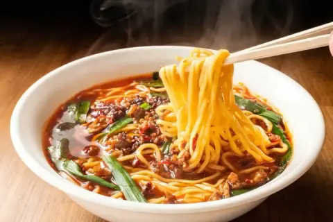 Gorący, parujący ramen z mięsem mielonym i szczypiorkiem. Pałeczki unoszą kłębek żółtego makaronu, zapowiadając, jak smakuje ramen.