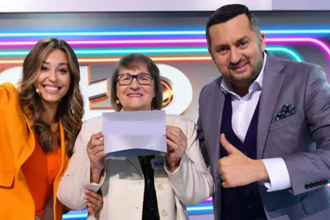 Trzy osoby: kobieta w pomarańczowej marynarce, starsza kobieta z kartką i mężczyzna w garniturze pokazujący kciuk w górę.