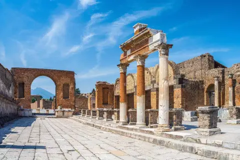 Ruines antiques de Pompéi sous un ciel bleu. Colonnes imposantes et un arc de brique invitent à visiter Pompéi et à imaginer la vie d'autrefois.