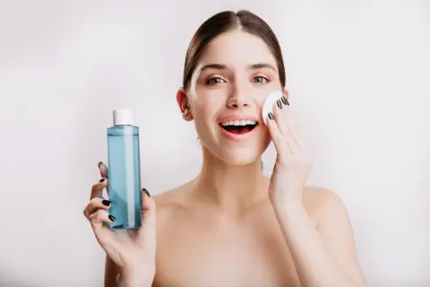 Mujer sonriente se aplica agua micelar Deliplus con un algodón. Piel radiante y fresca.