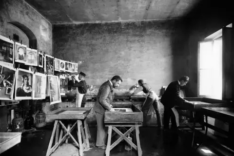 Alessandro Bardi e collaboratori lavorano in un laboratorio di stampa, con stampe appese e vasche per il trattamento.