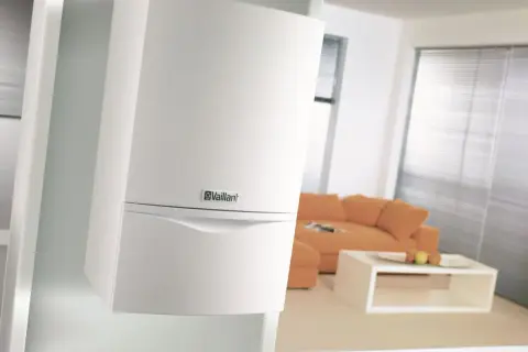 Nowoczesny, biały piec z zamkniętą komorą spalania marki Vaillant, dyskretnie zamontowany na ścianie w salonie.