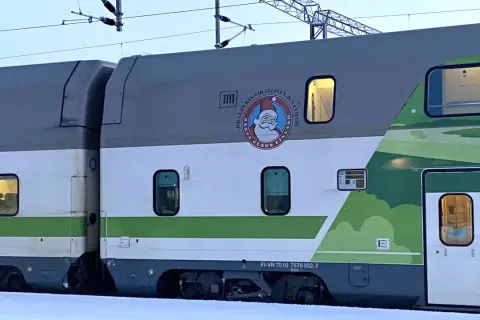 Ein Nachtzug mit Weihnachtsmann-Logo und grüner Landschaftsdekoration im Schnee.