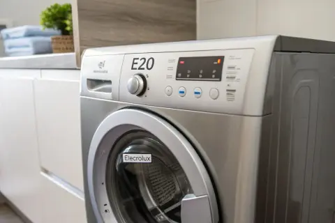 Pralka Electrolux z wyświetlonym błędem E20. Na blacie obok stoją złożone ręczniki i roślina.
