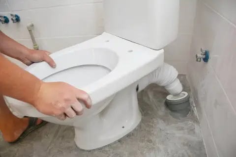 Installation d'un nouveau WC. Les mains ajustent le siège pour une évacuation WC parfaite.