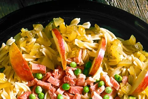 En närbild på en läcker pastasallad med skinka, äppelklyftor och gröna ärtor. En perfekt sommarmåltid!