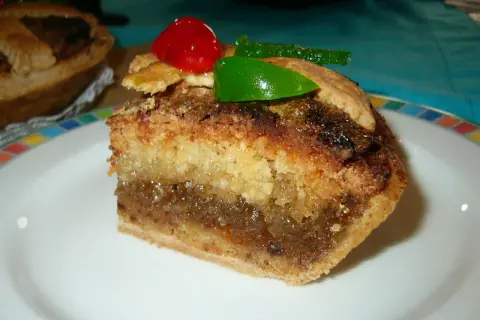 Rebanada de tarta de Mondoñedo, con capas de bizcocho y relleno dulce, decorada con una cereza y un trozo de fruta escarchada verde.
