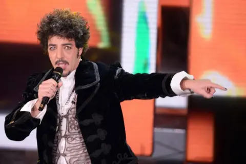 Max Gazzè canta con microfono, vestito elegante, con un'espressione intensa. Sembra che stia raccontando storie con i suoi testi, come se fosse "sotto casa".