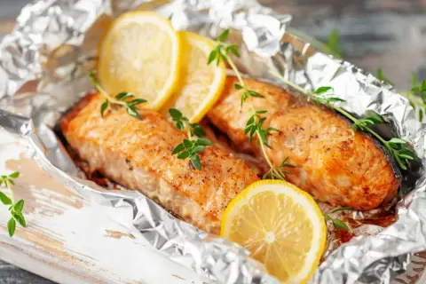 Deux pavés de saumon en papillote, ornés de rondelles de citron et de brins de thym frais, prêts à être dégustés.