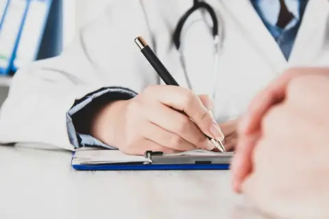 Lekarz pisze na dokumentach, zastanawiając się, czy zwolnienie od psychiatry zostaje w papierach.