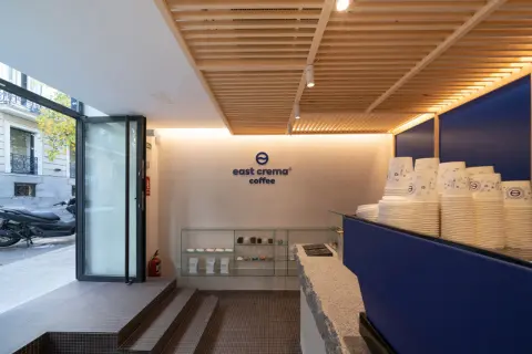 Interior de cafetería con logo "east crema coffee", vasos apilados y estanterías con productos.