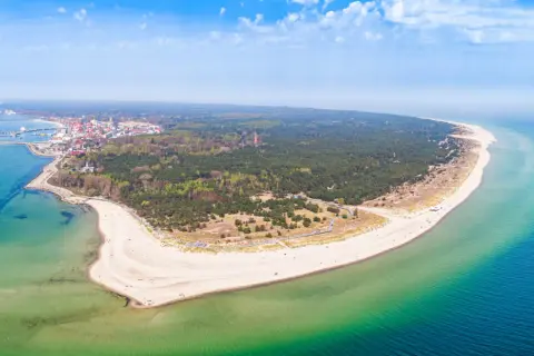Malownicze wybrzeże pomorza gdańskiego z piaszczystą plażą, lasem sosnowym i miasteczkiem nad zatoką.