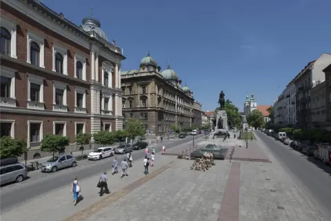 Kraków: pomnik Grunwaldzki, zabytkowe budynki i spacerujący ludzie. Wśród nich można sobie wyobrazić znane osoby z Krakowa.