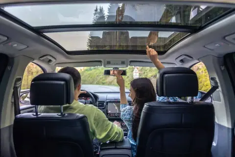 Familie im Auto mit Panoramadach. Die Sonne scheint durch das Fenster, hoffentlich kein Sonnenbrand!