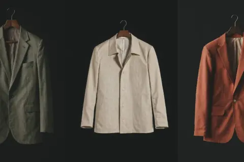 Drei Sakkos in Olivgrün, Beige und Rostrot hängen an Kleiderbügeln. Sie repräsentieren die **slow fashion definition**: zeitlose Designs, hochwertige Materialien und Langlebigkeit.
