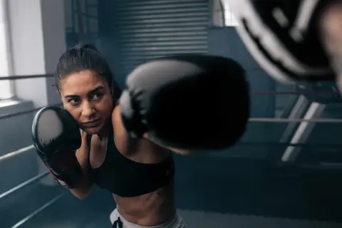 A woman in boxing gloves throws a punch in a ring. She looks focused, channeling her energy. Does boxing help with anger? This image suggests it can be a powerful outlet.