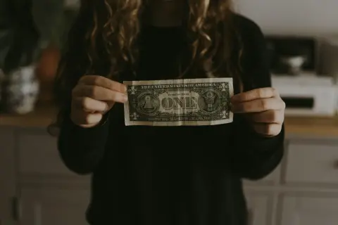 Dłoń trzyma banknot jednodolarowy, symbolizujący początek budowania majątku.