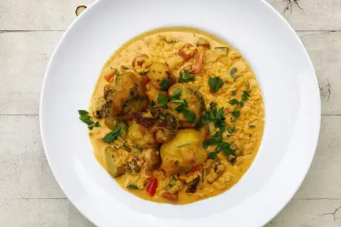Pyszny ryż z curry z warzywami i kawałkami kurczaka, posypany świeżą natką pietruszki.