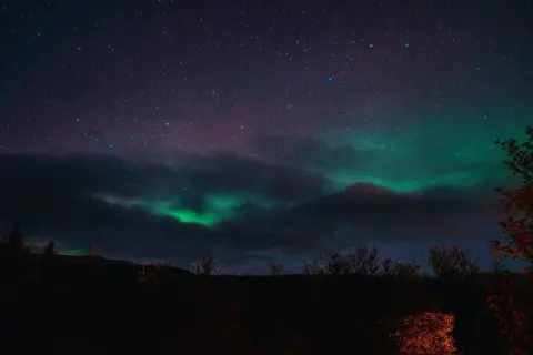 Zielona zorza polarna tańczy na nocnym niebie nad Islandią, wśród gwiazd i ciemnych chmur.