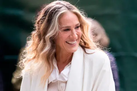 Mujer sonríe con cabello rubio y castaño con técnica reverse balayage, luciendo un abrigo blanco.