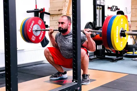Man utför en djup knäböj med skivstång, en klassisk övning som en del av sin russian squat routine.