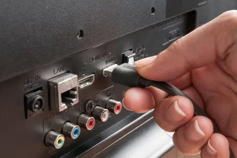Dłoń podłącza kabel do portu HDMI ARC w telewizorze, obok złącza LAN.