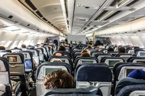 Blick in den Gang eines Flugzeugs. Viele Passagiere sitzen auf ihren Plätzen im Flugzeug innen, einige schauen auf die Bildschirme vor sich.