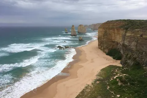 Piękne klify i plaża nad oceanem, kiedy w Australii jest lato. Woda jest turkusowa, a fale rozbijają się o brzeg.