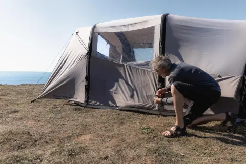 Mężczyzna rozbija namiot na trawiastym klifie nad morzem. Czy można rozbić namiot na plaży? To miejsce wygląda idealnie.