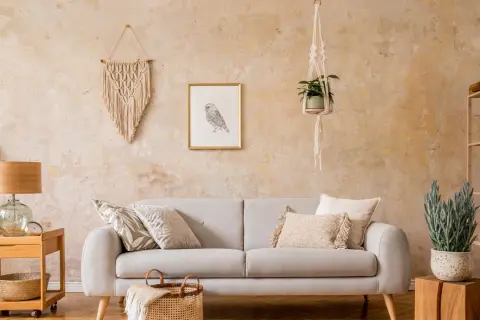 Gemütliches Wohnzimmer mit beiger Couch, Makramee-Wandbehang und einer Wand in Wischtechnik.