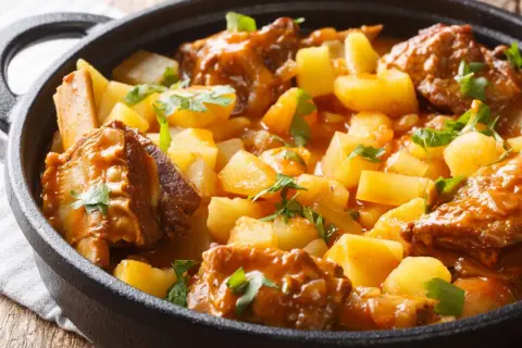 Un reconfortante guiso de patatas con costillas, cubierto de perejil fresco, servido en una olla de hierro fundido.
