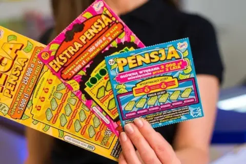 Kobieta trzyma zdrapki lotto z hasłem "Ekstra Pensja". Tabela wygranych pokazuje szansę na dużą wygraną.