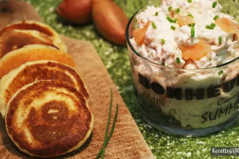 Petits blinis dorés accompagnant un délicieux verre de rillettes de saumon, parsemé de ciboulette fraîche.