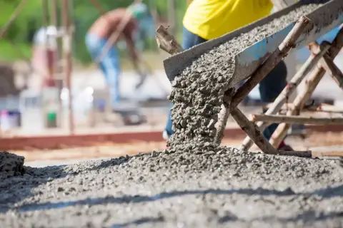 Betoniarka wylewa świeży beton. Pracownicy na budowie dbają o odpowiednią ilość cementu na kubik betonu, by zapewnić trwałość konstrukcji.