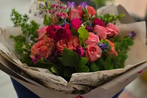 Piękny bukiet różowych i czerwonych róż, ozdobiony zielenią i drobnymi fioletowymi kwiatkami. Idealne kwiaty dla mamy, by sprawić jej radość.