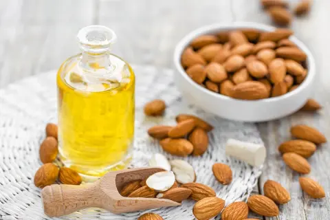 Aceite de almendras en botella, almendras en cuenco y esparcidas. El aceite de almendras mancha la piel con el sol, ¡pero nutre!