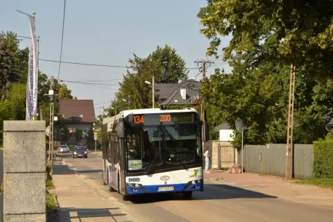 Autobus linii 134 z napisem "ZOO" jedzie ulicą w Krakowie, wśród zieleni i domów.