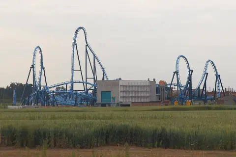 Niebieska kolejka górska Energylandia Abyssus z pętlami i zakrętami na tle pola zboża i budynków.