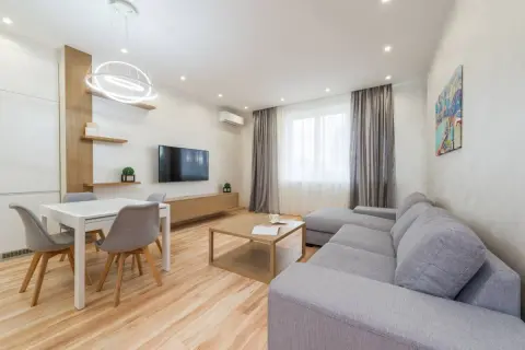 Elegante salón con sofá gris, mesa de comedor blanca y detalles en madera. Los colores del salón crean un ambiente acogedor y moderno.