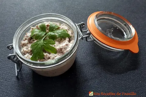 Un bocal ouvert révèle de délicieuses rillettes de sardines, garnies d'une feuille de persil frais.