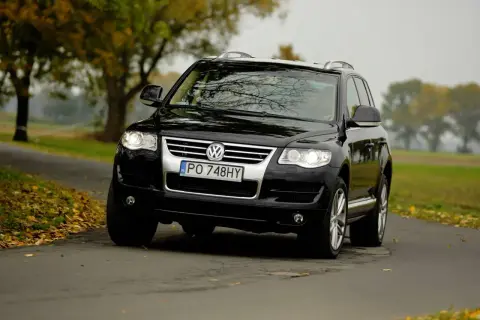 Czarny Volkswagen Touareg 2024 na jesiennej drodze, otoczony drzewami z kolorowymi liśćmi.