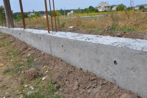 Betonowy fundament z prętami zbrojeniowymi. Czy można postawić płot przy płocie? Tu powstaje podstawa pod nowy.