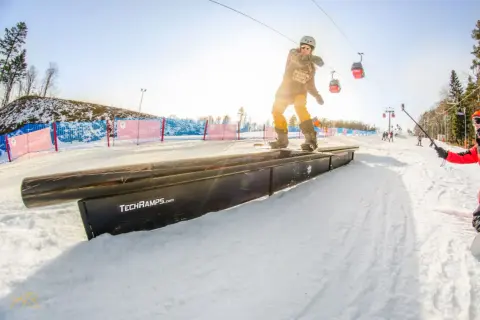 Snowboardzista na grindboxie w **Jaworzynie Krynickiej snowparku**. W tle kolejka linowa i inni narciarze.
