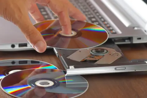 Dłoń wkłada płytę CD do napędu laptopa. Program cdburnerxp pomoże nagrać dane.
