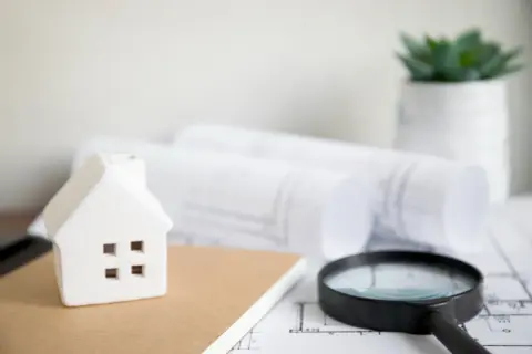 Modellino di casa, lente d'ingrandimento e progetti su un tavolo, pronti per un controllo edilizio.