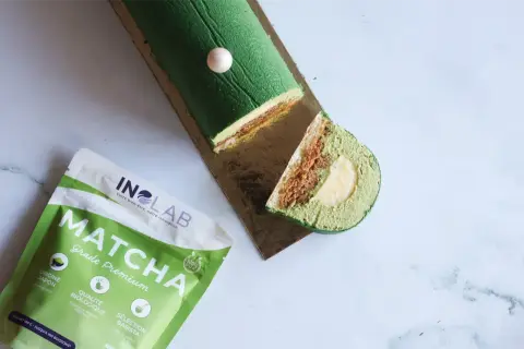 Bûche glacée verte au matcha, garnie d'une ganache matcha crémeuse et d'une surprise au centre. À côté, un paquet de poudre de matcha de qualité premium.
